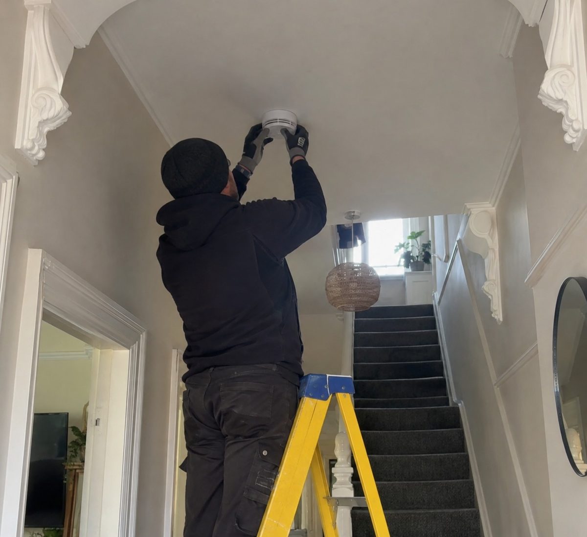 An alarm being fitted to a hallway ceiling