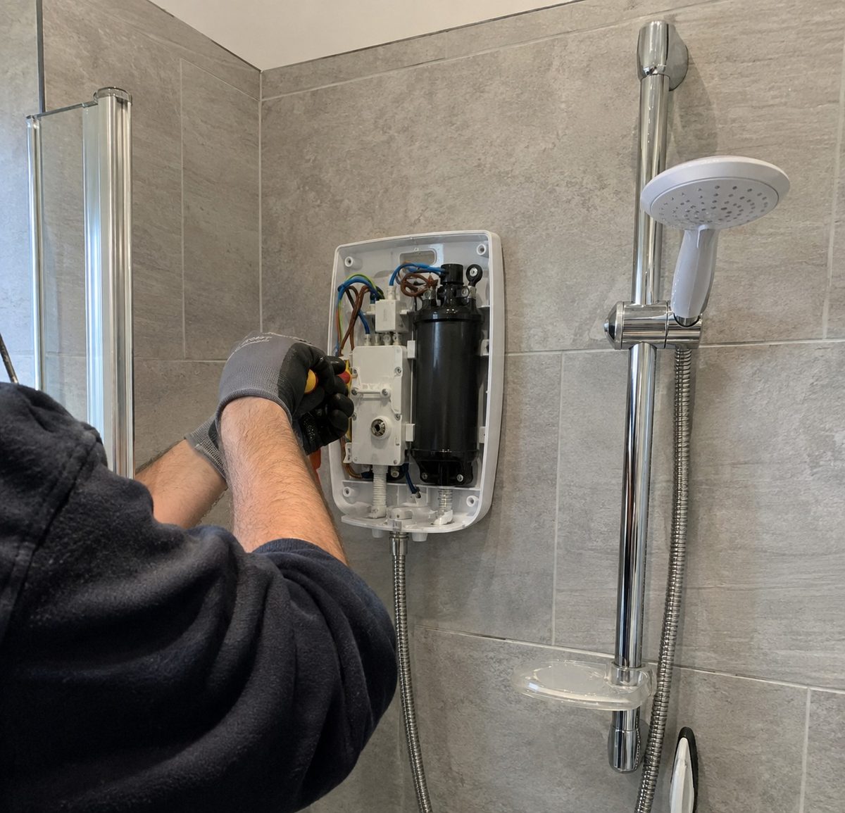 An electric shower unit being fitted to a tiled wall in a shower enclosure